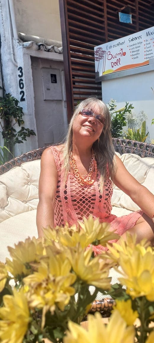 Dulce Helena sentada, sorrindo, com flores amarelas à frente